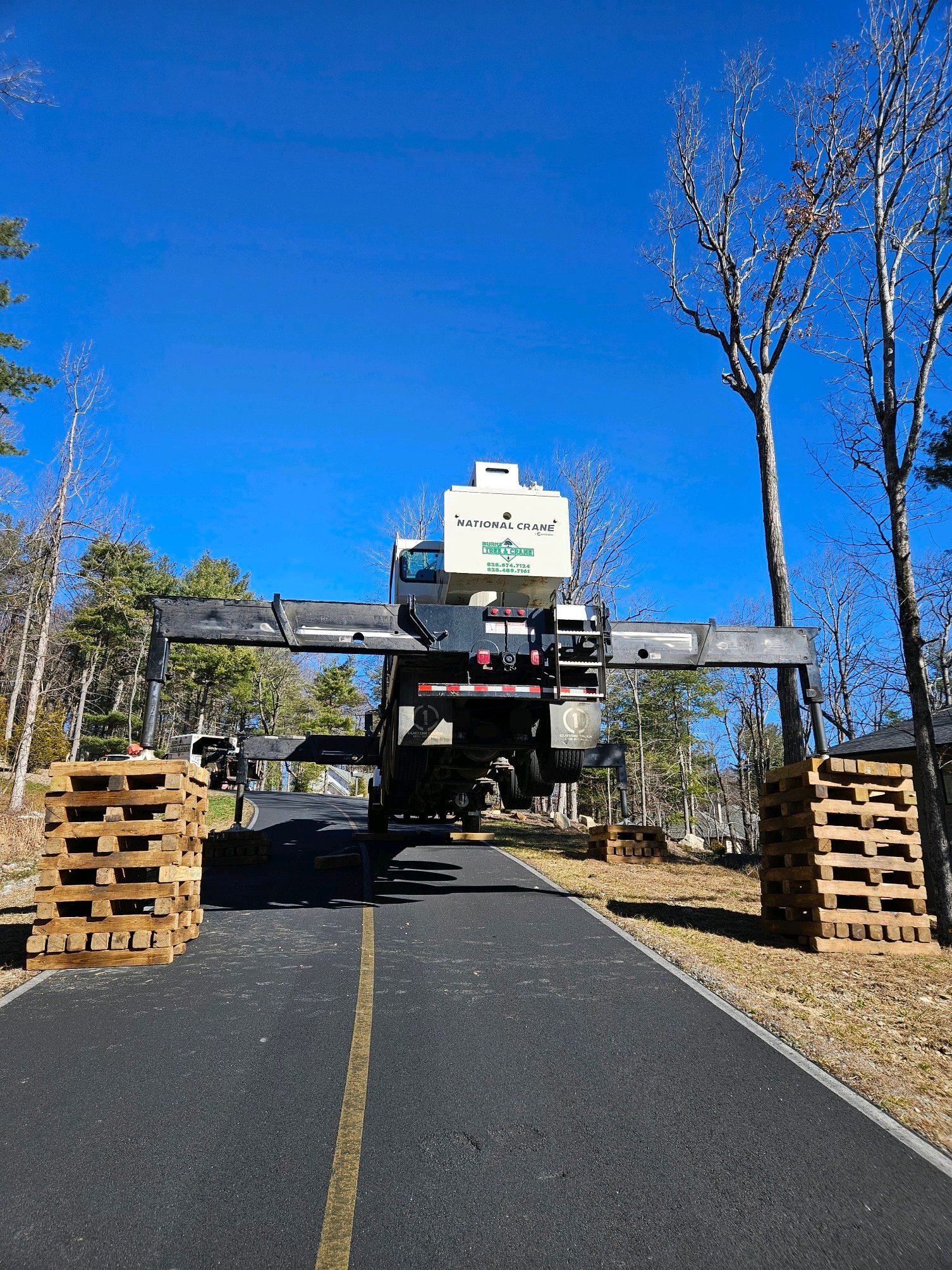 Gantry-style crane on road, wooden pallets on both sides, bright blue sky.