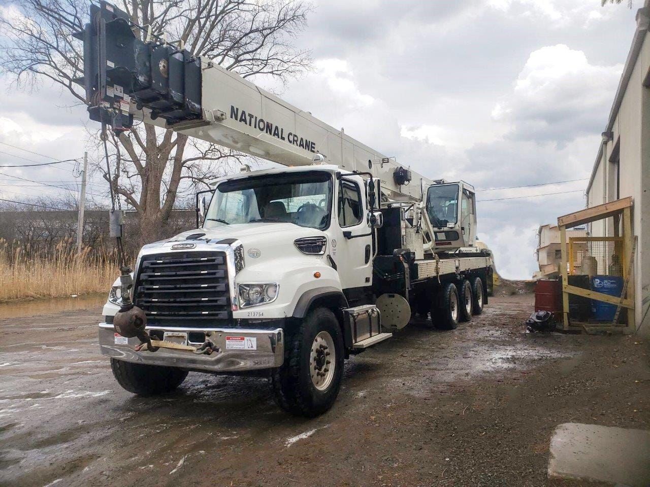 White National Crane truck parked on a wet surface with its boom extended, next to a building.