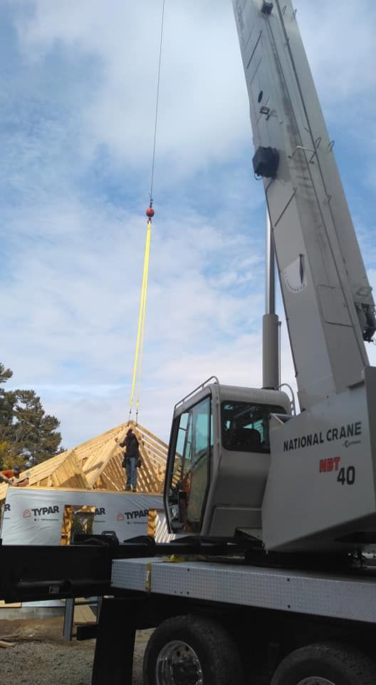 A crane lifts a wooden roof section over a construction site.