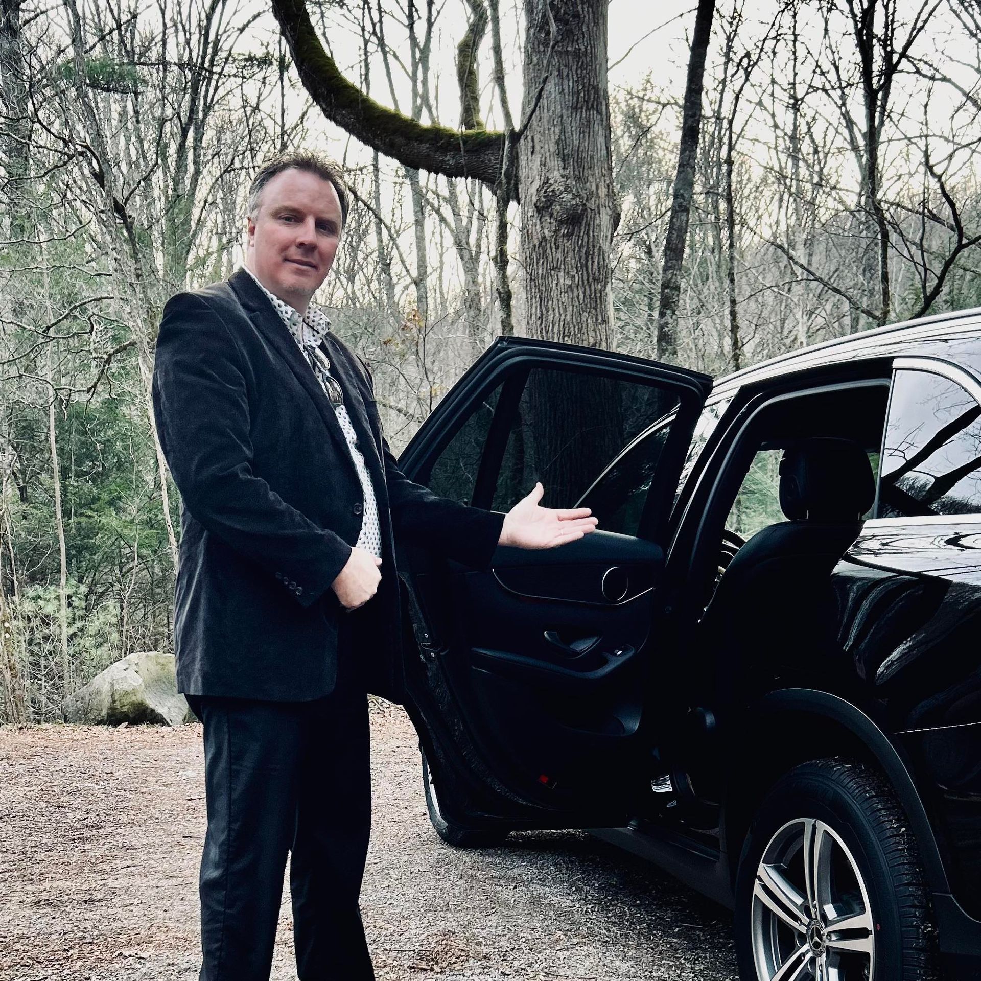 a man in a suit and tie is standing next to a black car .