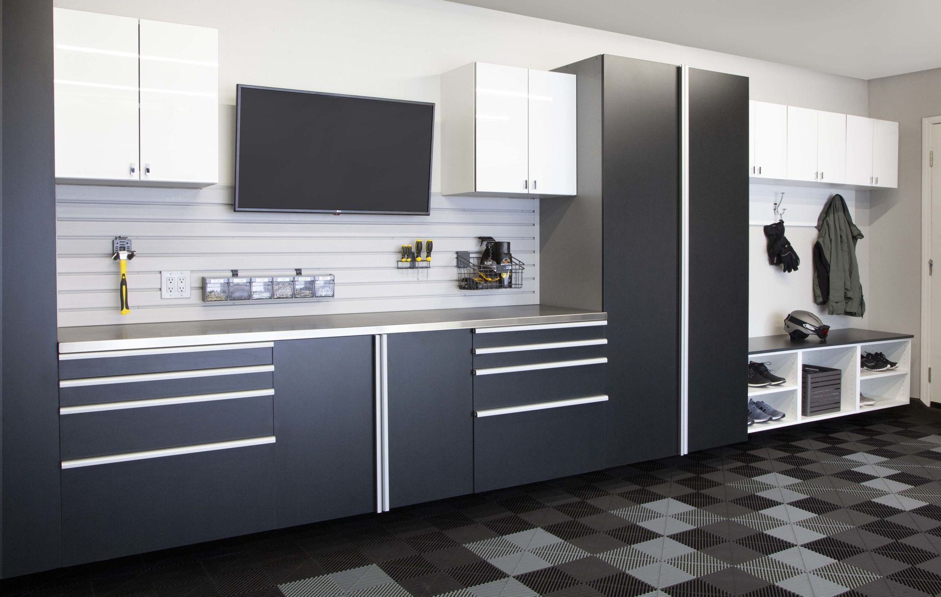 Modern garage storage with white and charcoal grey cabinets, a slat wall system, a workbench, and a mudroom bench area.
