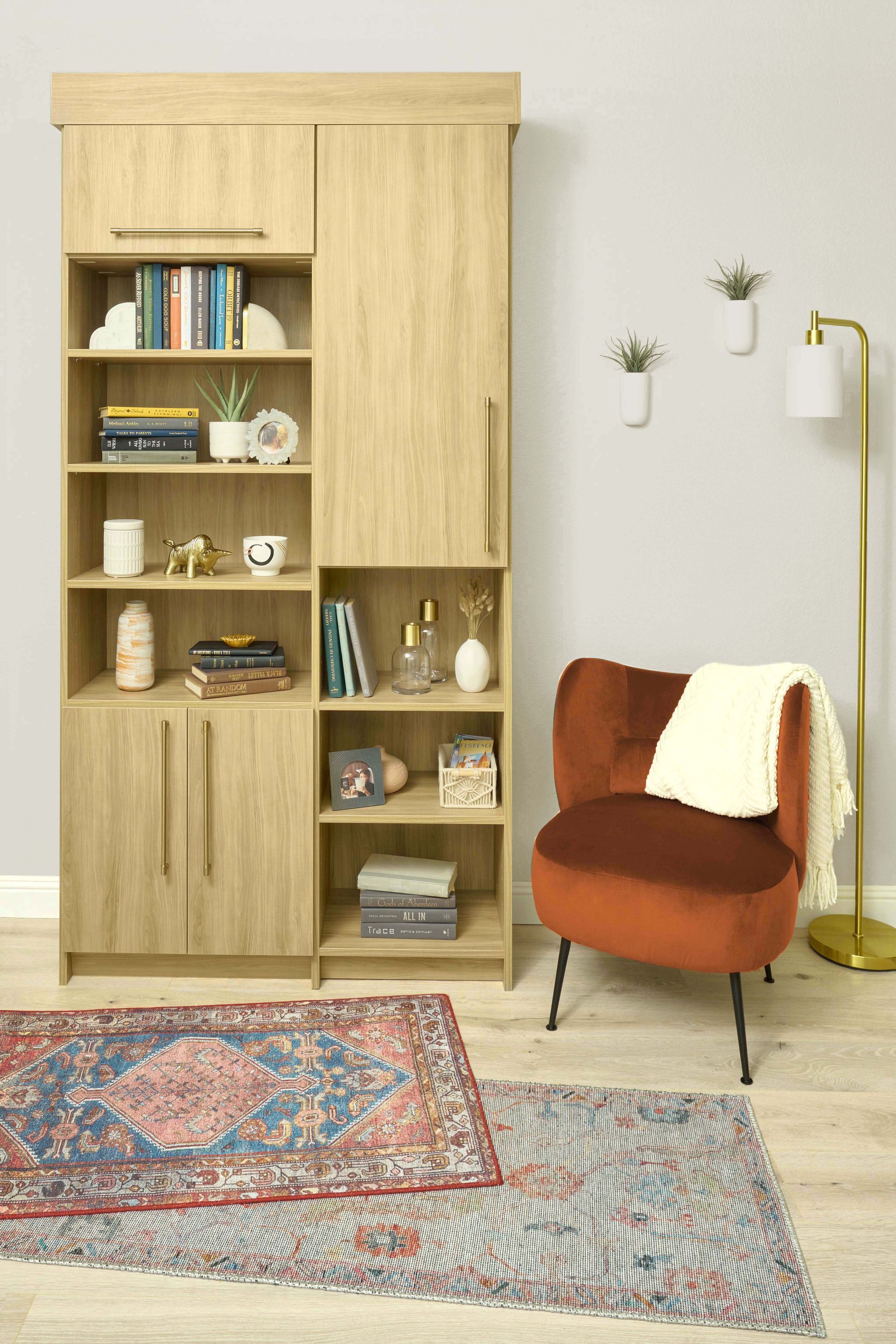 Wooden bookcase and orange chair in a bright living room with a patterned rug and floor lamp.