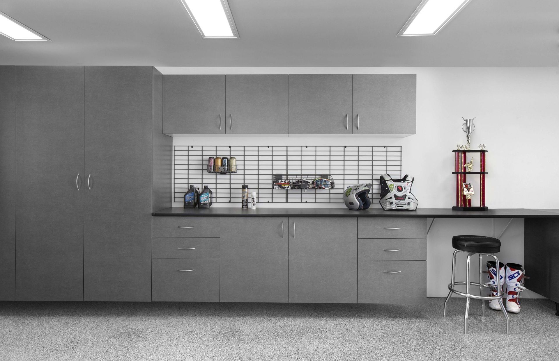 A gray garage storage system with upper and lower cabinets, a workbench, wall grid organizers, and a stool.