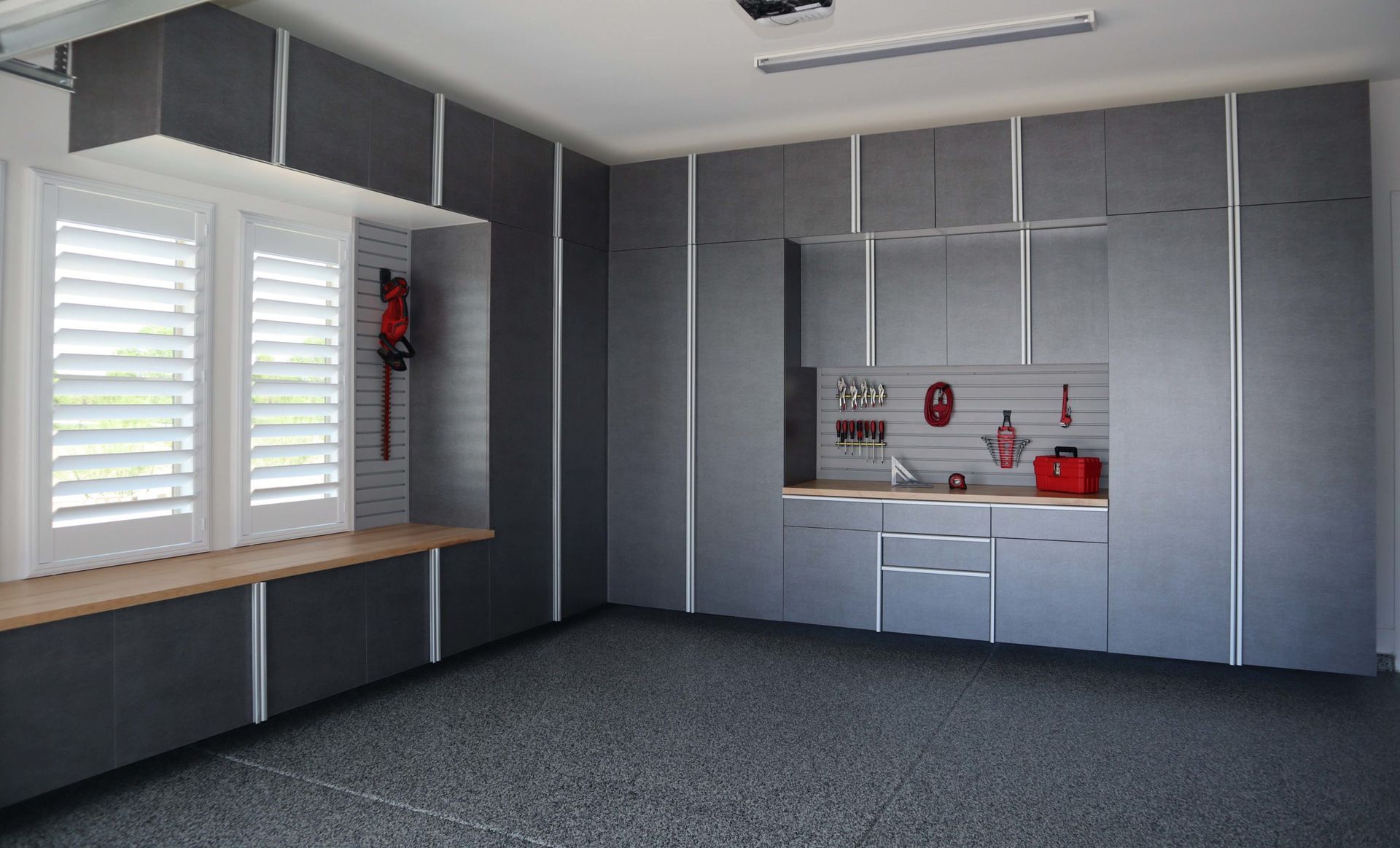 Modern garage interior with charcoal grey cabinetry, a workbench, and a window with white plantation shutters.