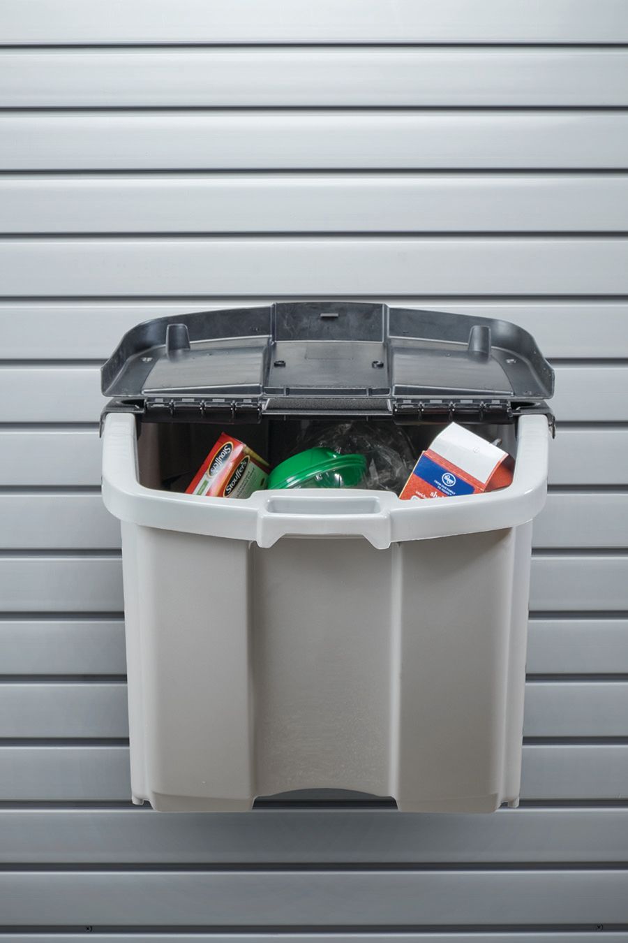 Partially open gray trash bin with garbage bags against a corrugated metal wall