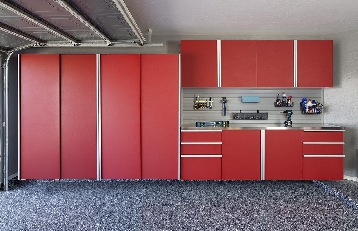Red wall-mounted cabinets and base storage units with drawers installed in a garage with grey speckled floors.