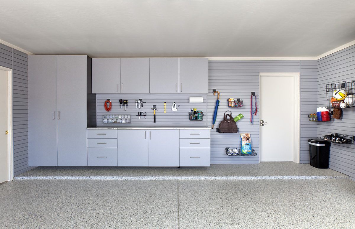 A garage with light gray cabinets, slat-wall storage, a workbench, and a speckled epoxy floor.