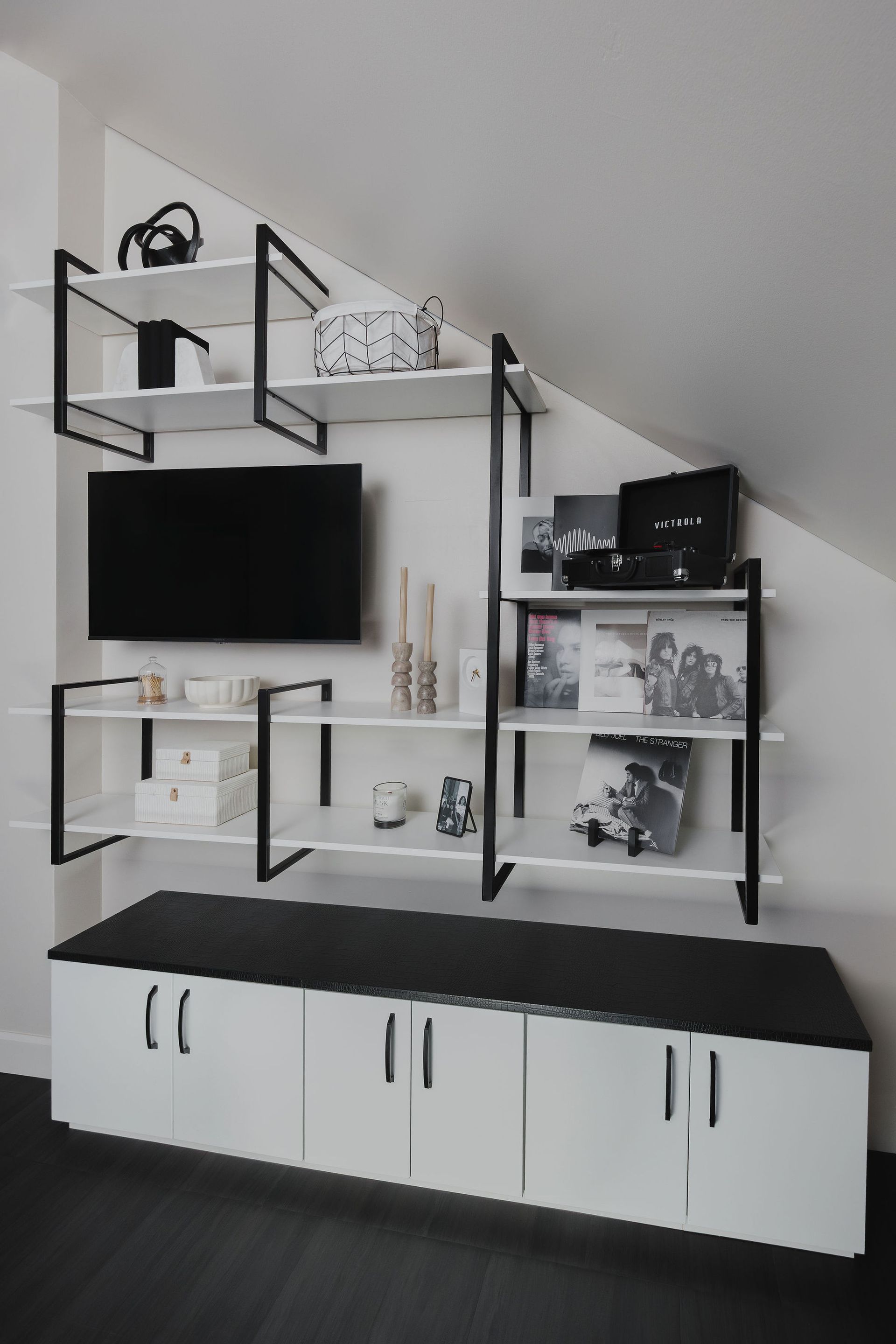 Modern black-and-white wall shelf unit with TV and cabinets in a slanted-ceiling room