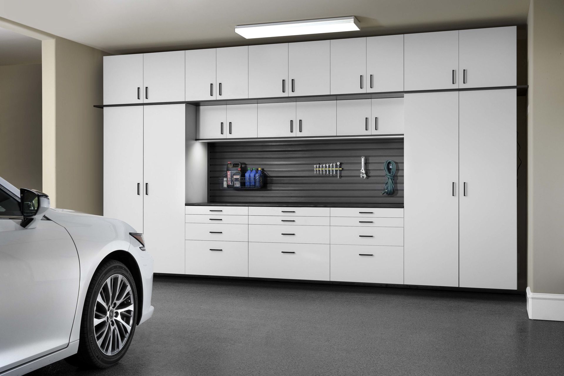 A wall of white garage cabinets featuring overhead cupboards, deep drawers, and a central slat-wall tool organizer.