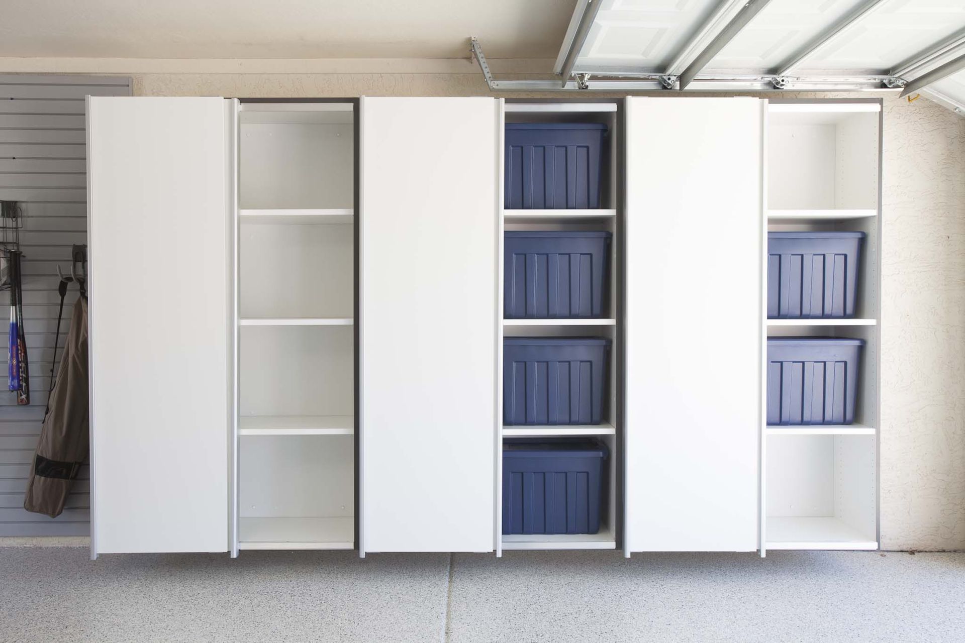 White storage cabinets in a garage featuring alternating sections of open shelving, some containing dark blue bins.