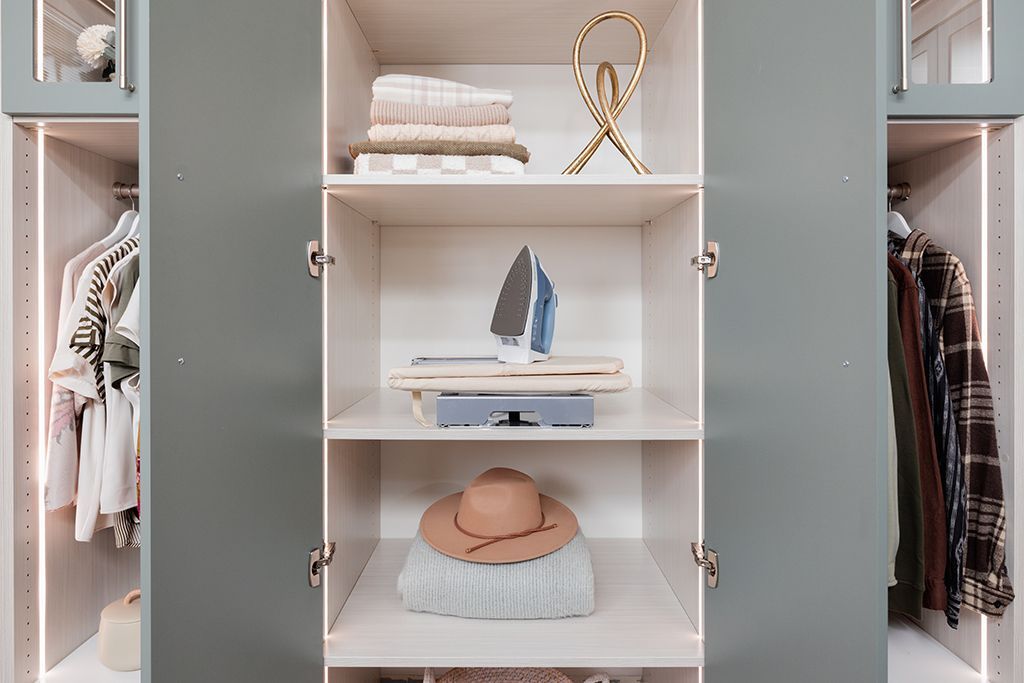 A closet filled with clothes and a boat on the shelf.