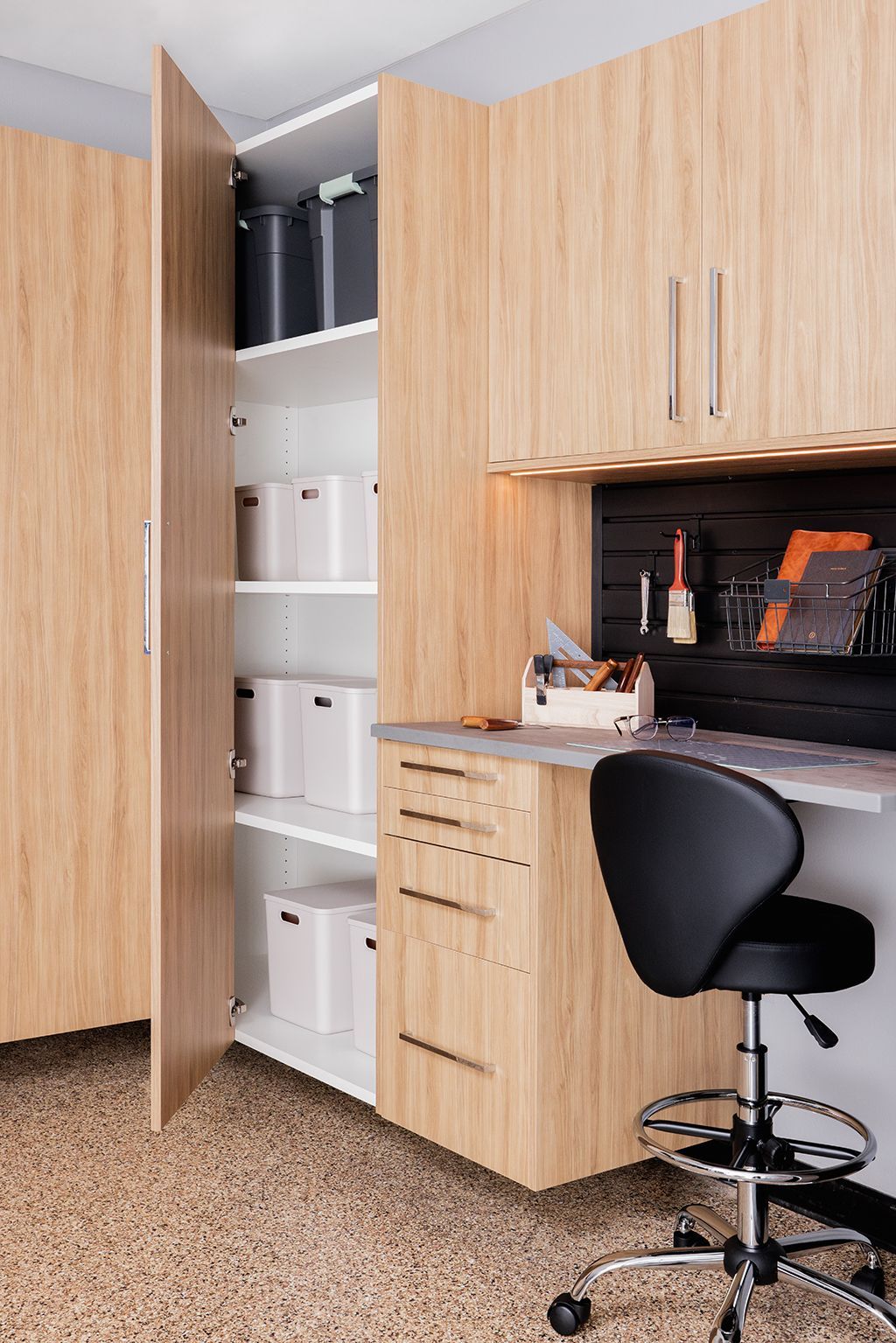 A garage with wooden cabinets , a desk and a chair.