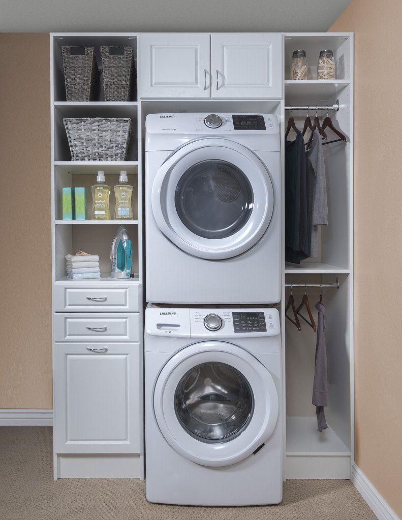 Stacked washer and dryer in white laundry cabinet with shelves, baskets, and hanging clothes