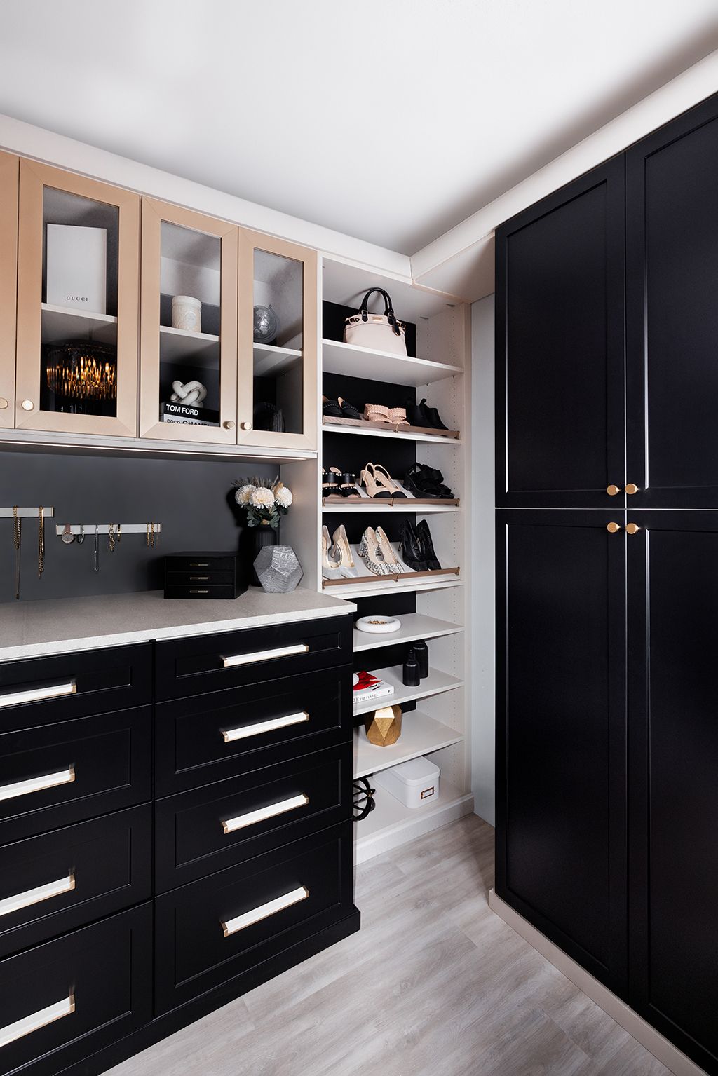 A walk in closet with black cabinets and shelves filled with shoes and handbags.