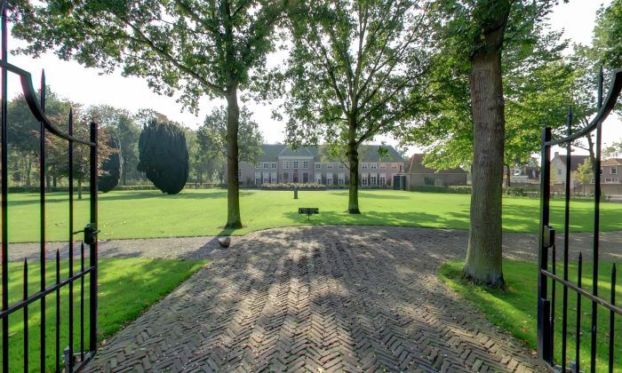 Een poort staat open naar een park met bomen en Stadspaleis Hotel OldRuitenborgh op de achtergrond.