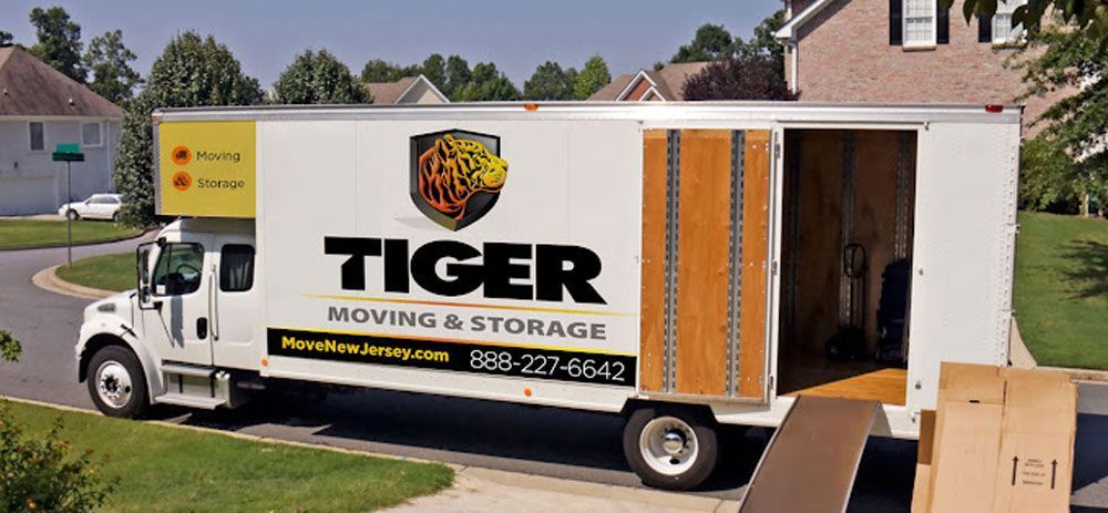 A tiger moving and storage truck is parked in front of a house.