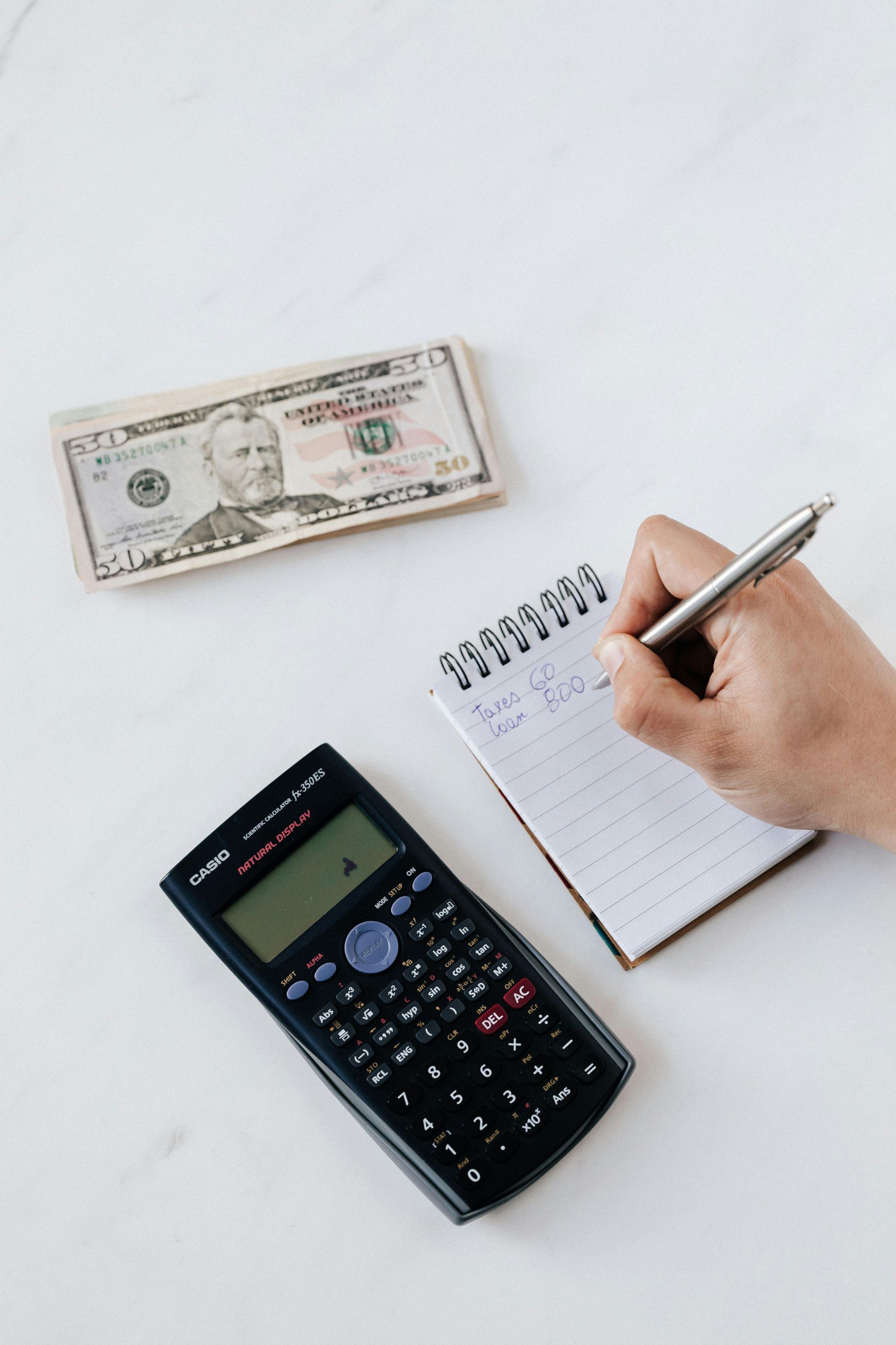 Roll of cash next to a calculator on a white surface.