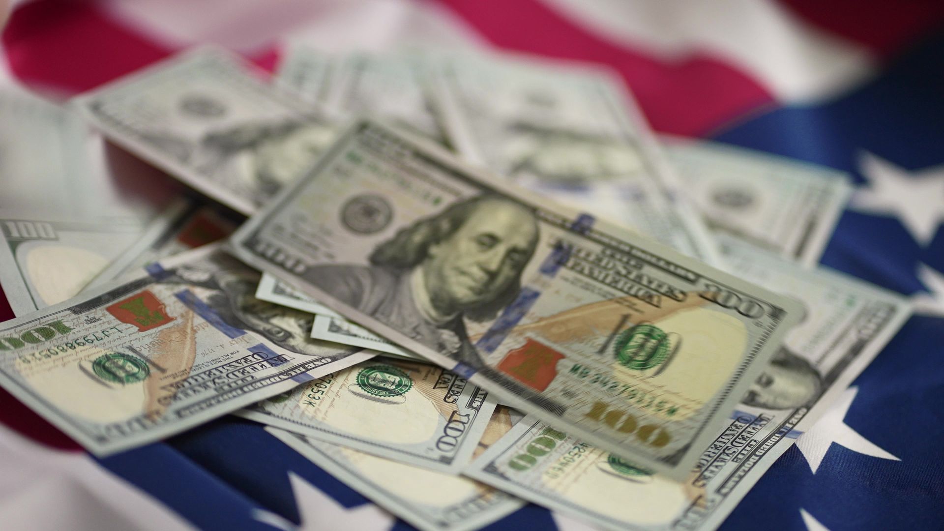 Pile of $100 bills on a red, white, and blue American flag.