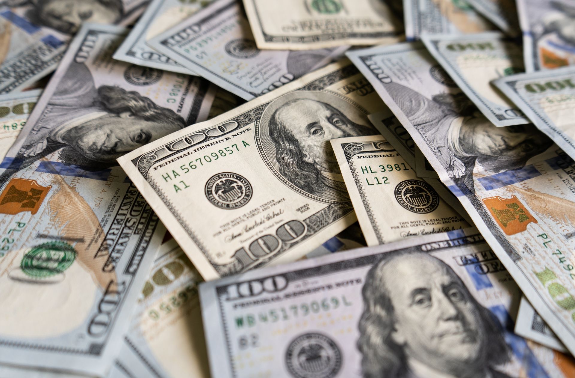 Pile of U.S. $100 bills, showing Benjamin Franklin's portrait, with slight focus on the center bills.