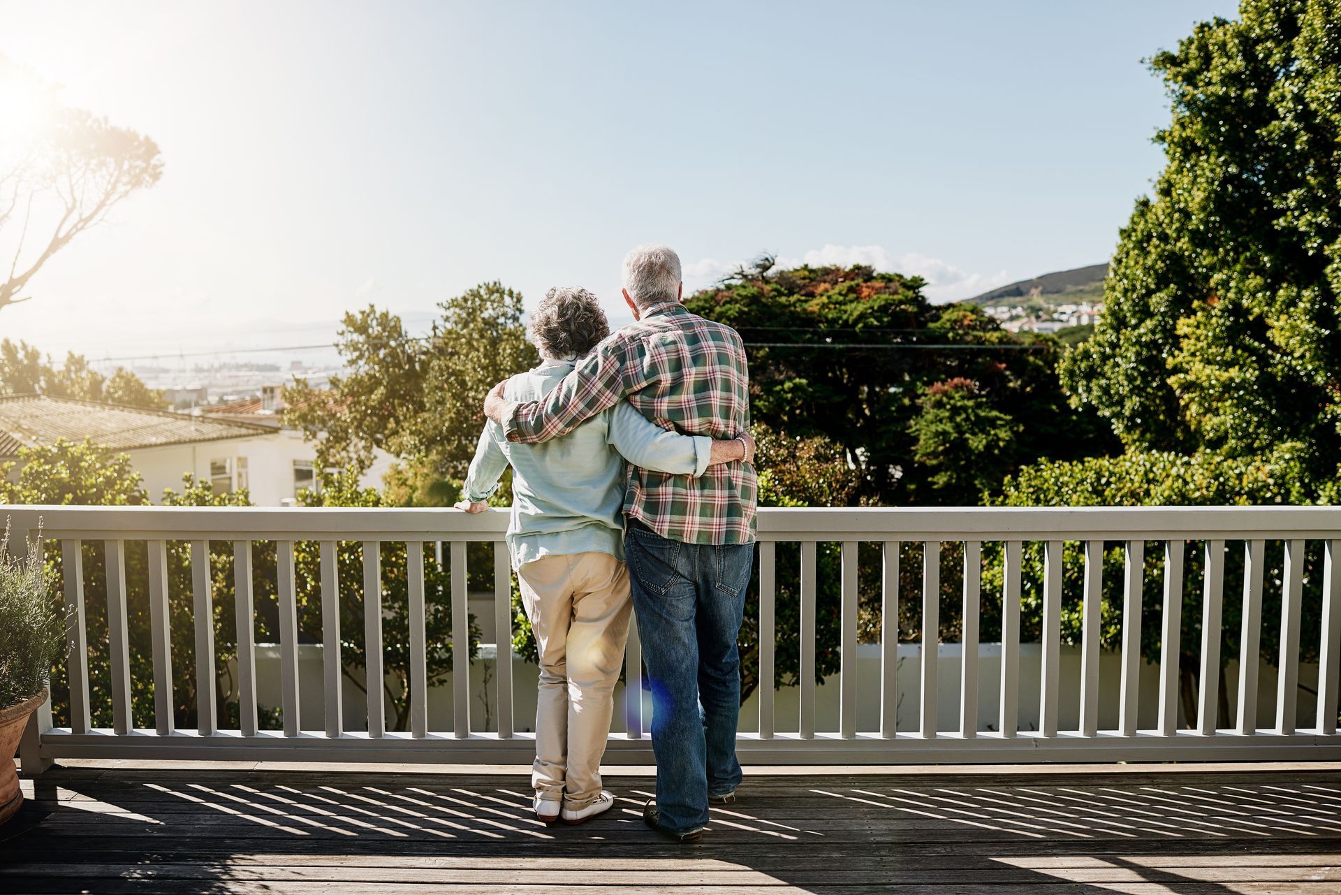 Couple with arms around each other, looking at a scenic view from a deck.