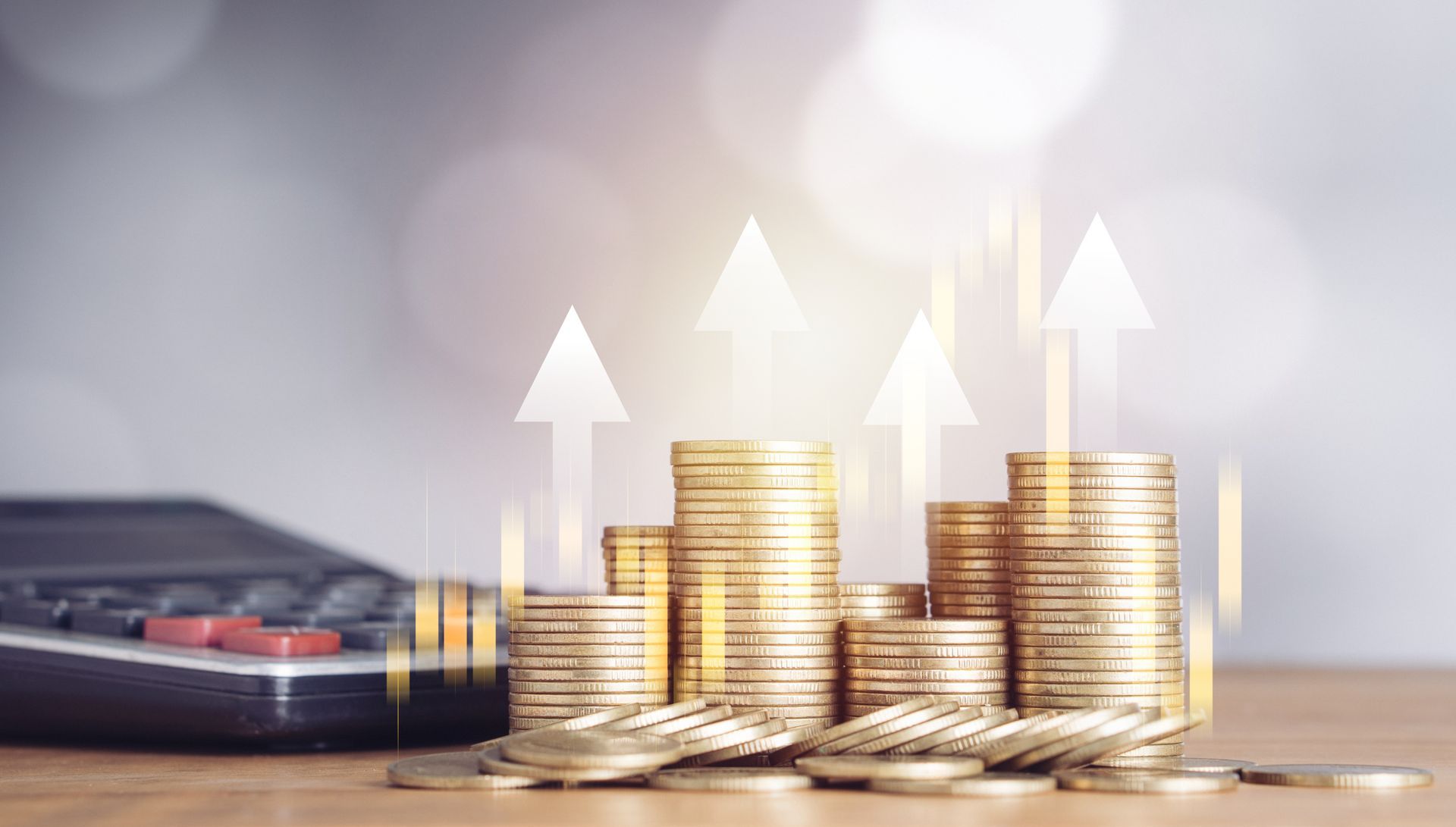 Stacks of gold coins with upward arrows, calculator in the background, representing financial growth.