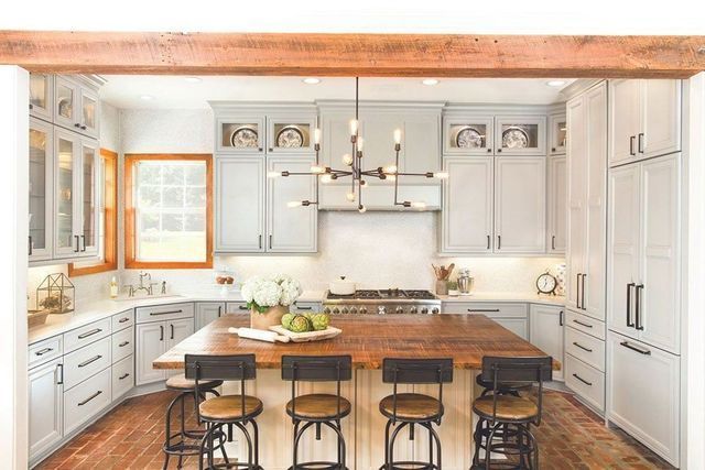 A kitchen with white cabinets , wooden floors , stools and a large island.