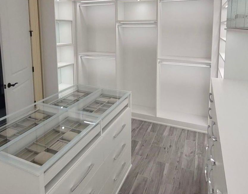 A walk in closet with white cabinets and a glass counter top.