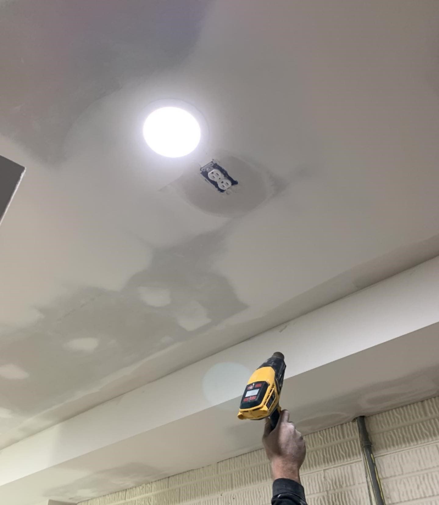A person is holding a drill in front of a ceiling.
