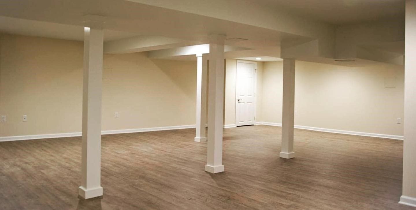An empty basement with wooden floors and white pillars.