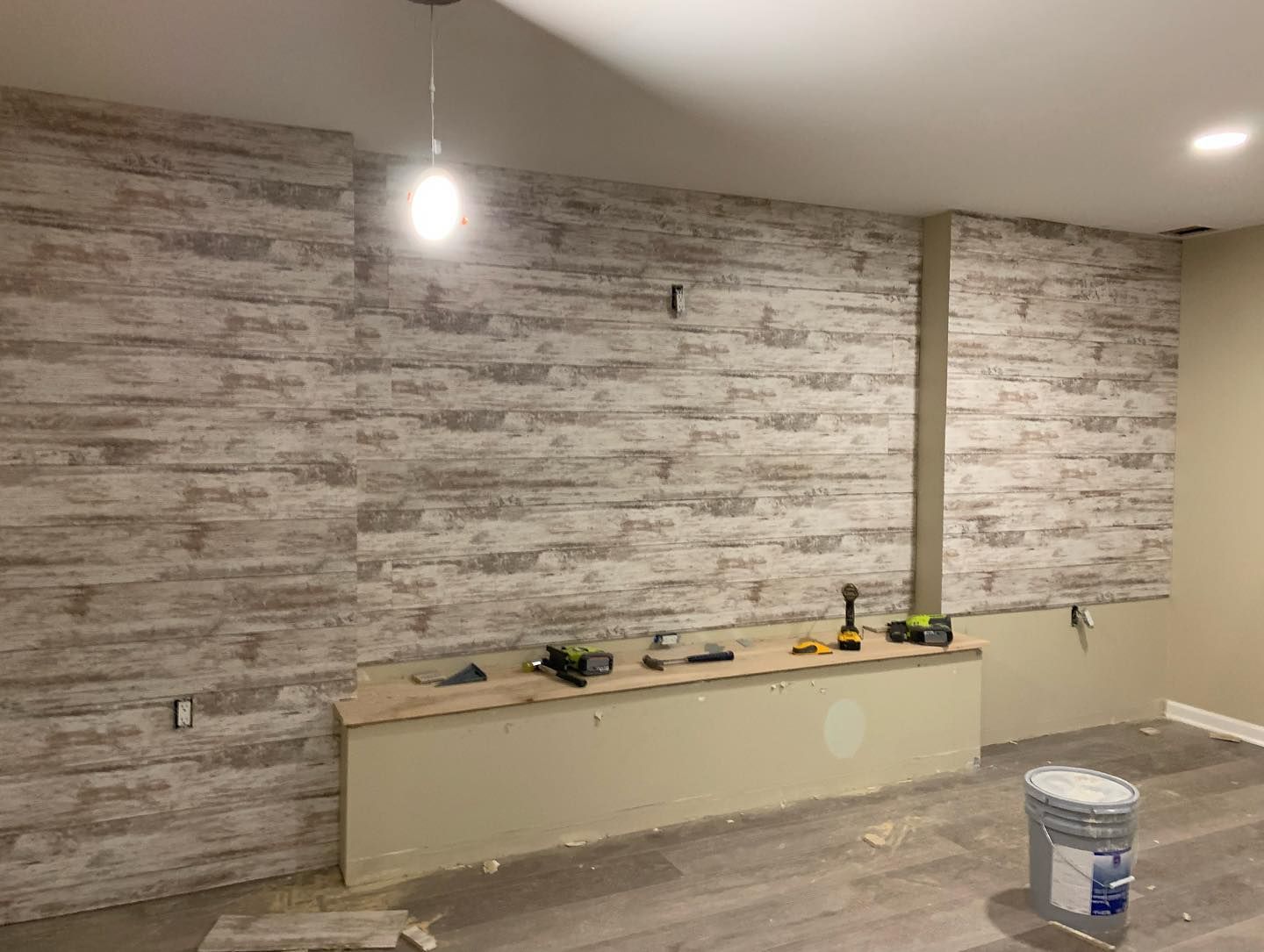 A room with a brick wall and a bucket of paint on the floor.