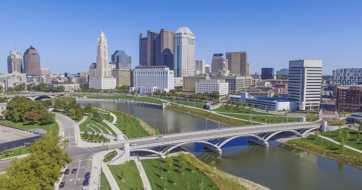 An aerial view of a city with a river in the foreground and a bridge in the background.