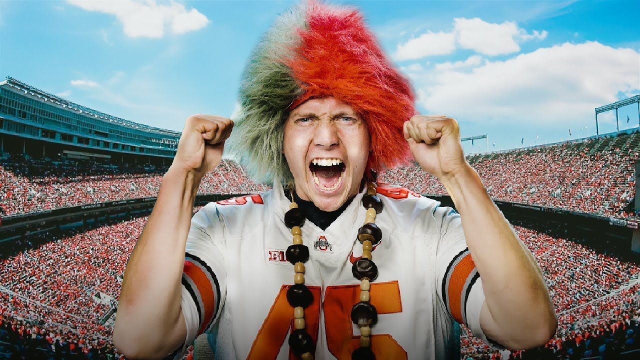 Cheering fan in red and green wig with raised fists in a crowded stadium