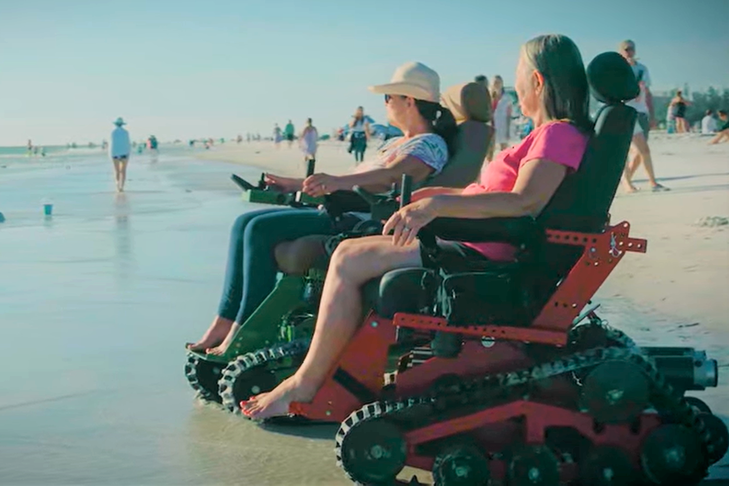 A group of people are sitting in wheelchairs on the beach.