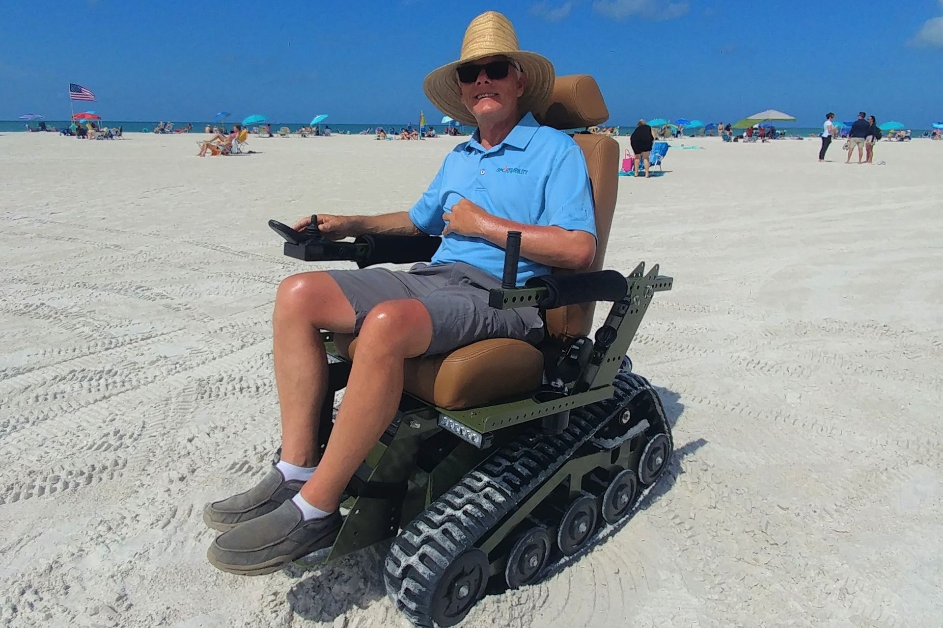 A man in a straw hat is sitting in a wheelchair on the beach.