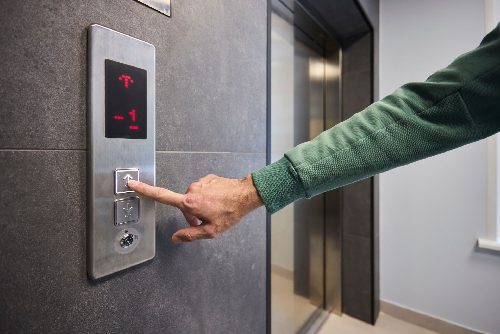 Hand pressing elevator button inside modern building lobby.