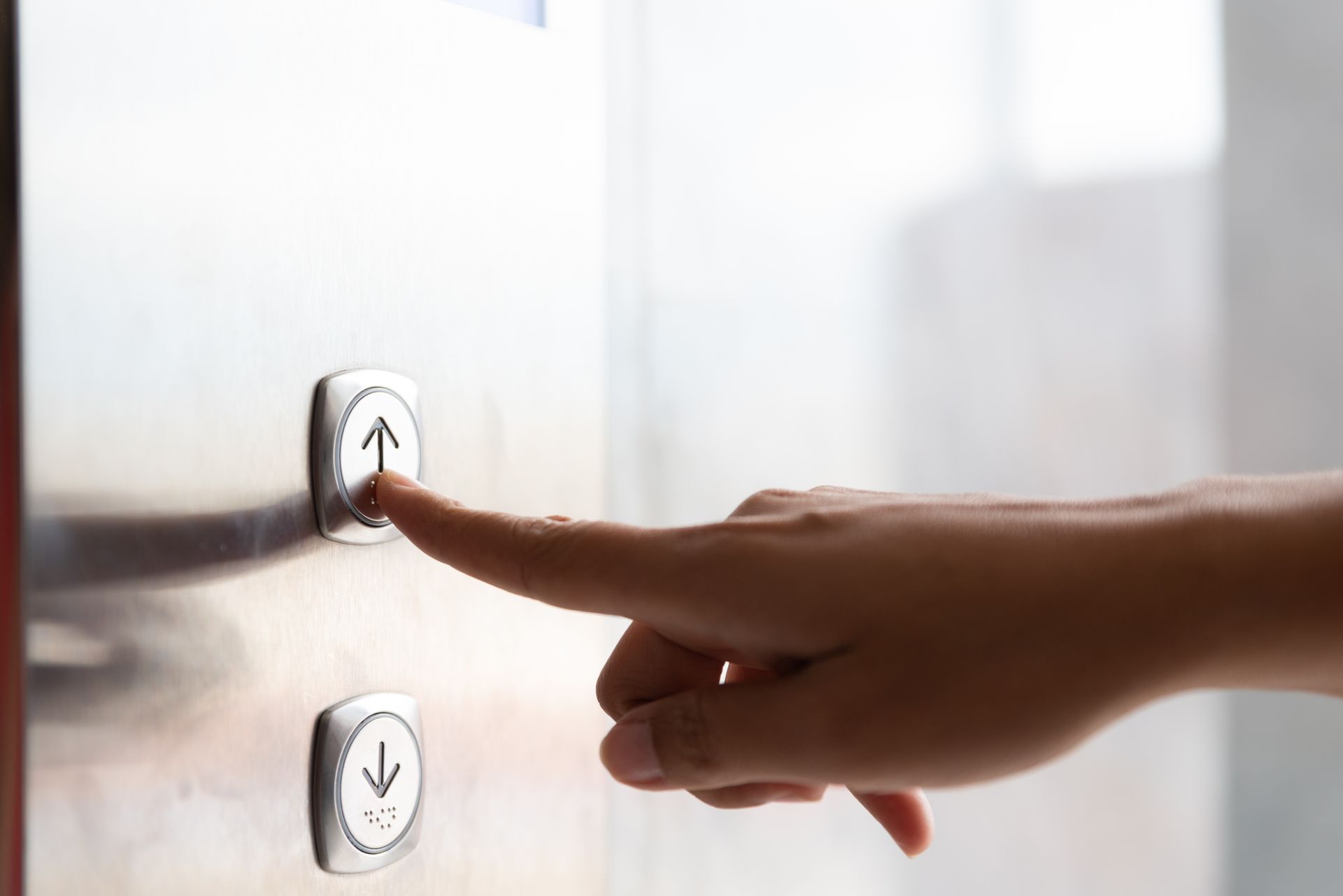 Finger pressing the up button on a wall mounted home elevator control panel.