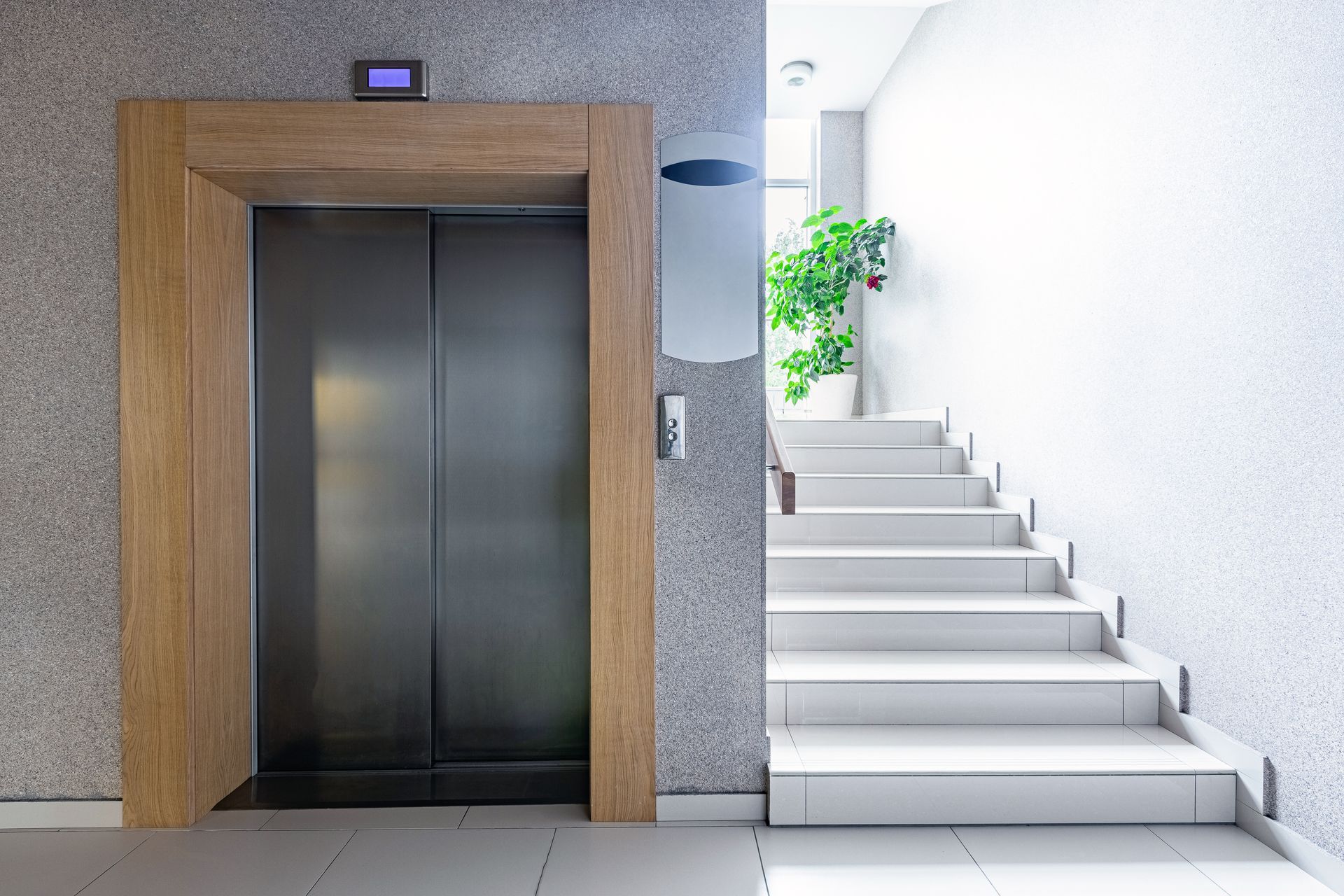 Modern wood-frame elevator beside bright stairs, minimalist with natural light.