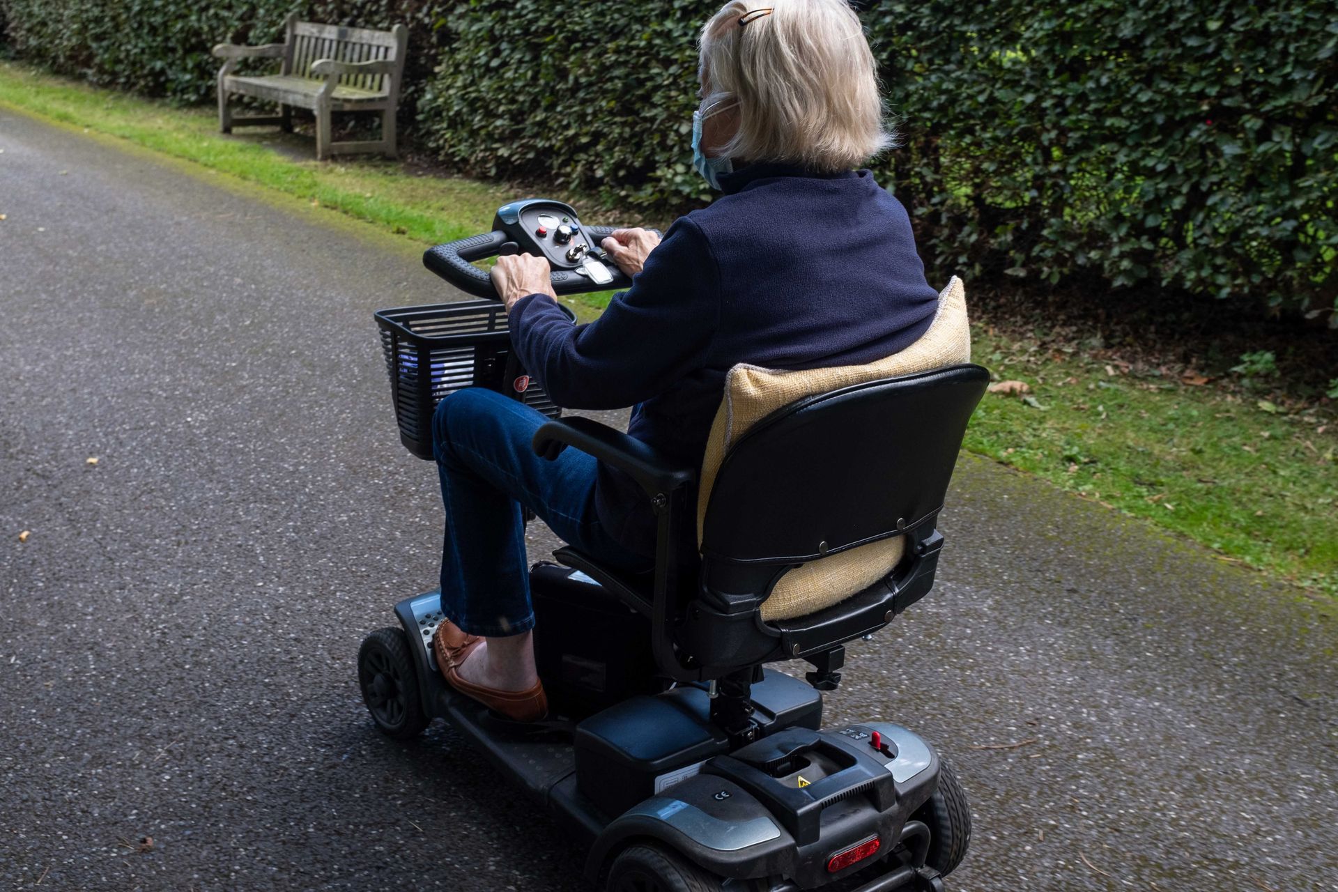 An old lady riding a mobility scooter on a quiet lane from behind three quarters view. An old lady riding a mobility scooter on a quiet lane from behind three quarters view.