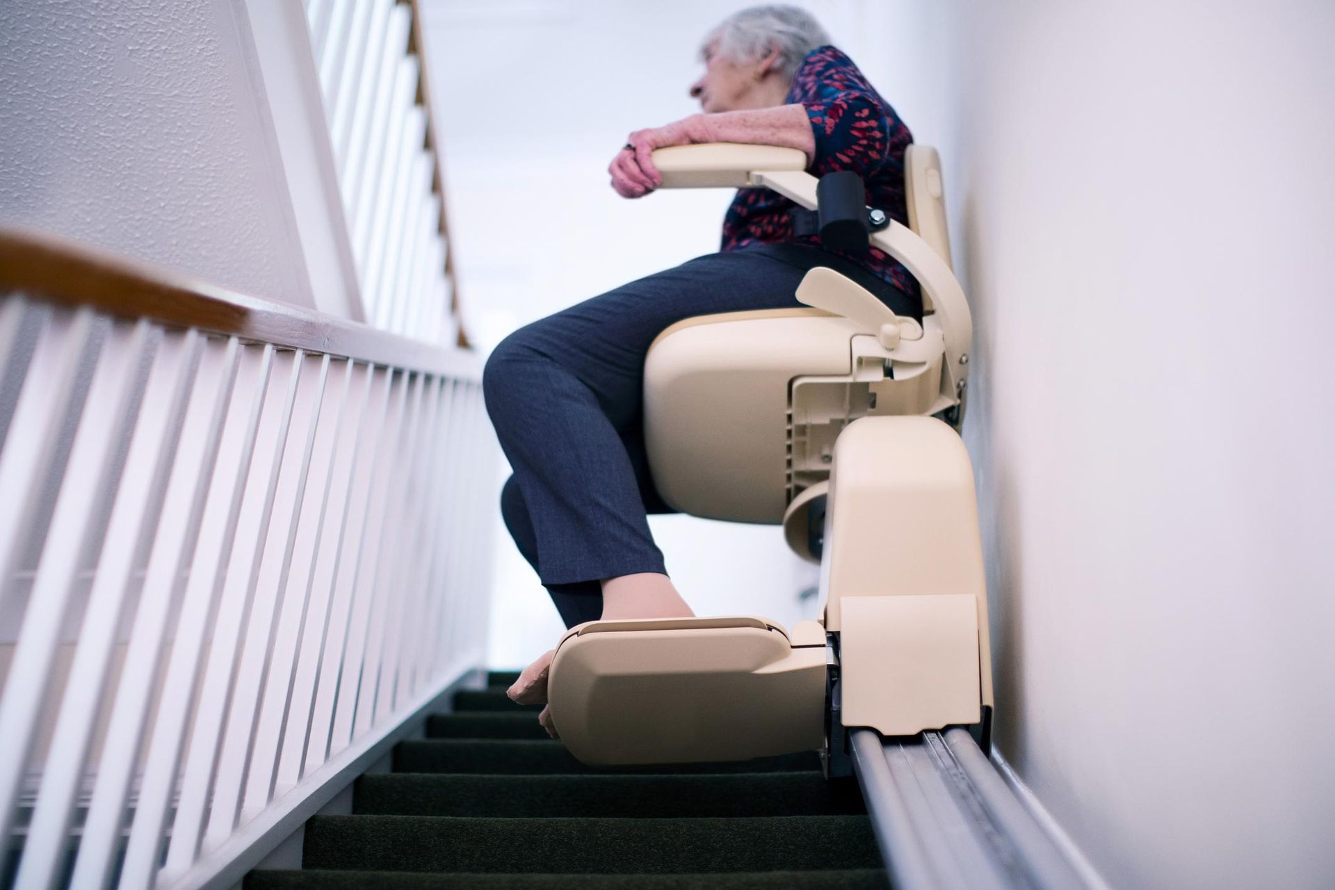 Elderly woman riding stairlift up home staircase for senior mobility assistance.