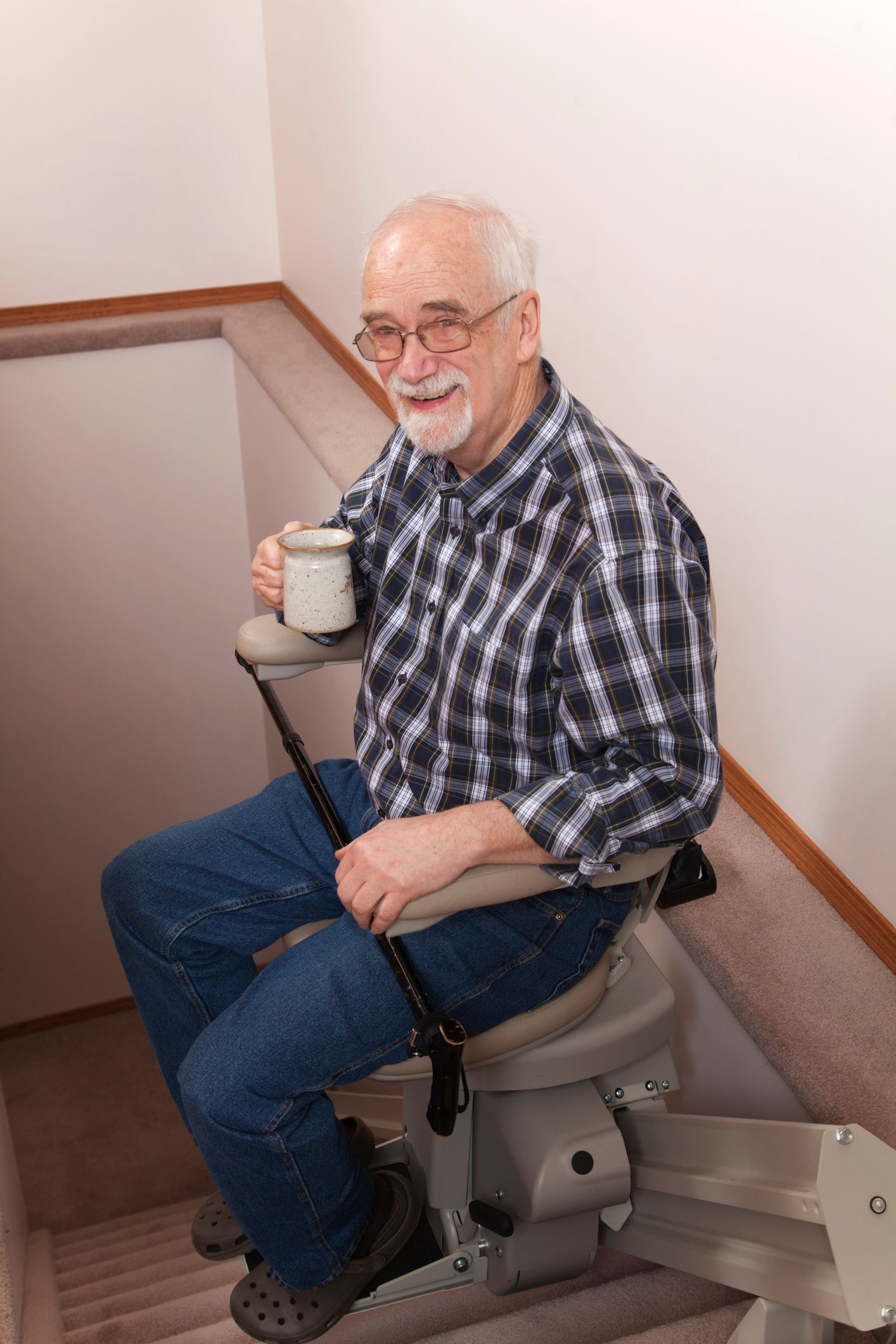 A male senior sits on a stair lift while smiling and holding a ceramic cup.