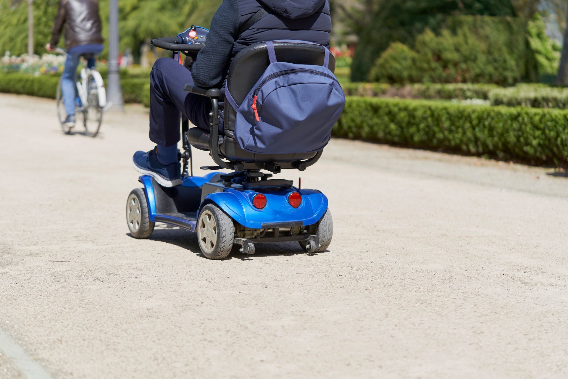 Person riding a four-wheel mobility scooter on a park path.] 