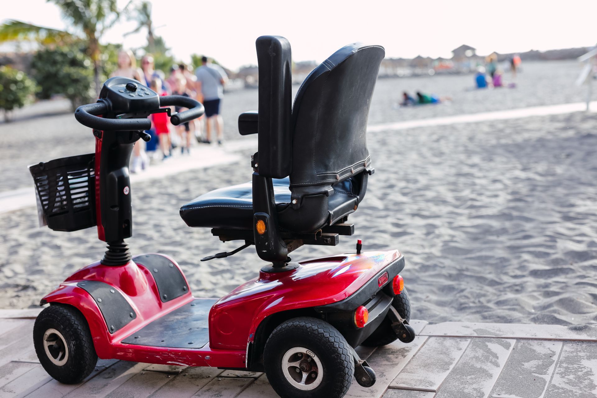 A red mobility scooter is parked on the sidewalk next to the beach.