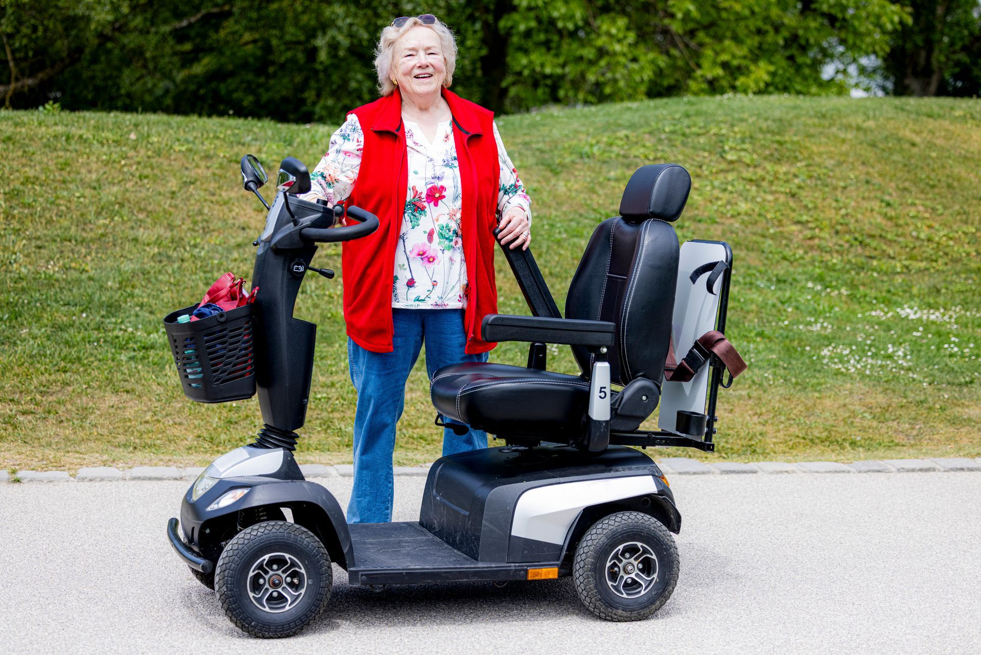 Senior woman stands prod behind her mobility scooter bought at a certified motor scooter dealer.