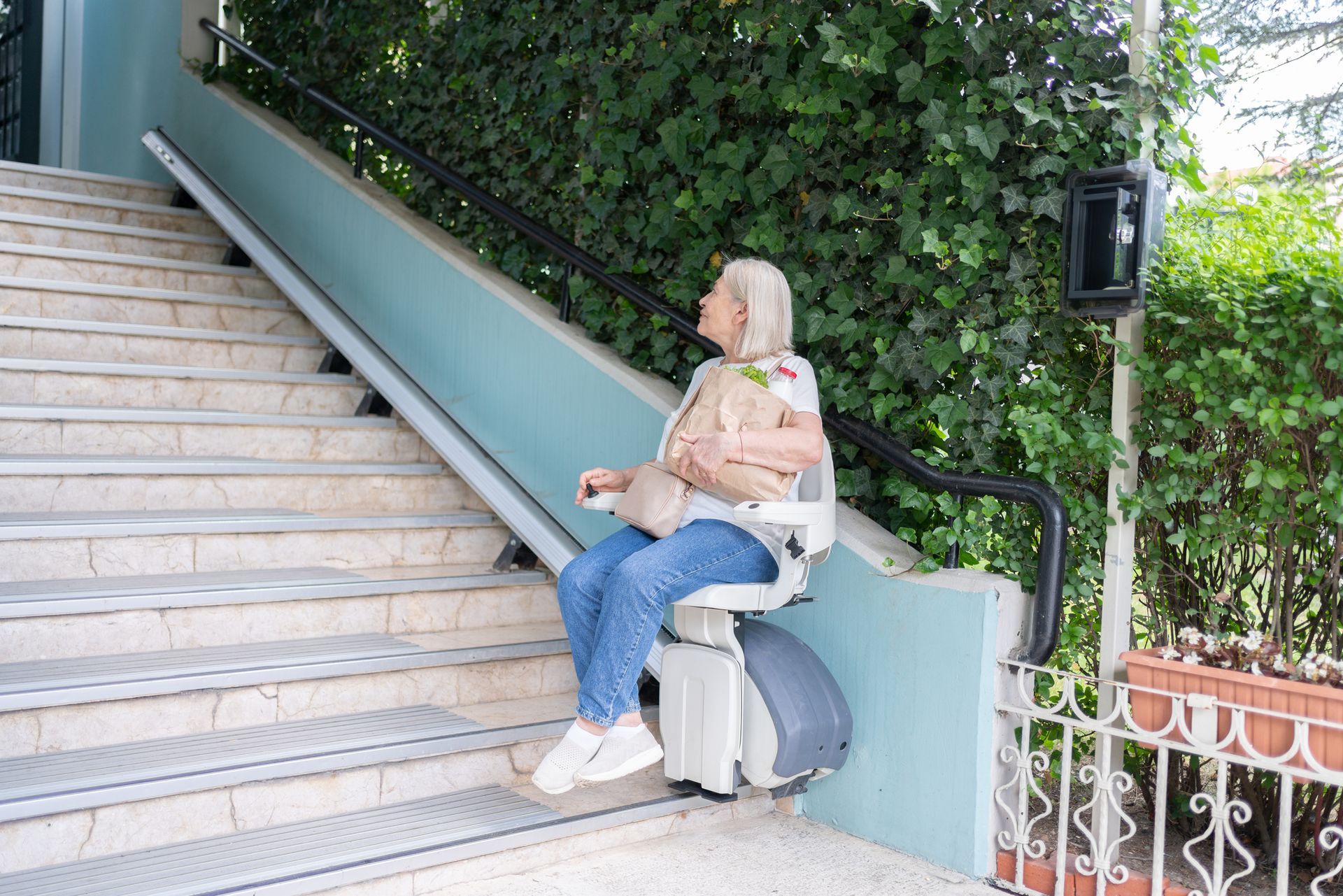 Senior woman using automatic chairlift on a staircase at the apartment entrance.