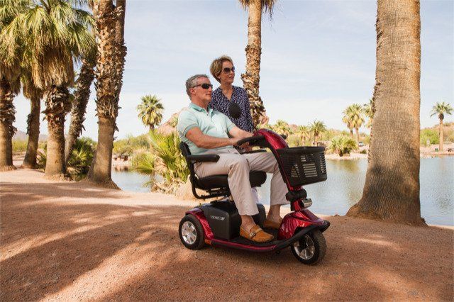 A man and woman are riding a mobility scooter next to a lake.