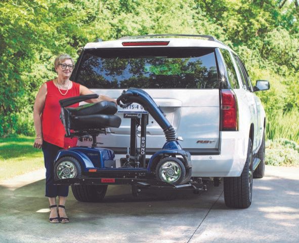 A woman is standing next to a mobility scooter attached to the back of a car