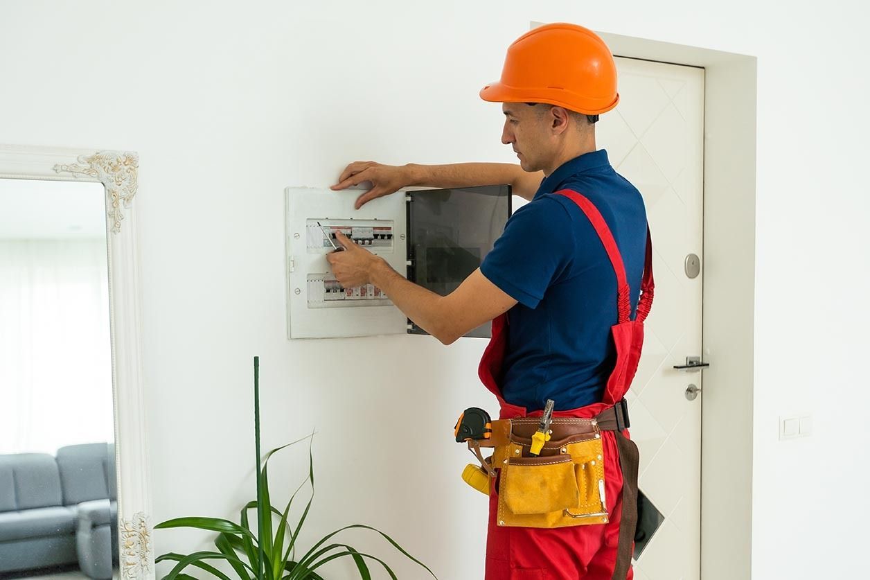 Electrician in orange hard hat adjusting a wall control panel indoors