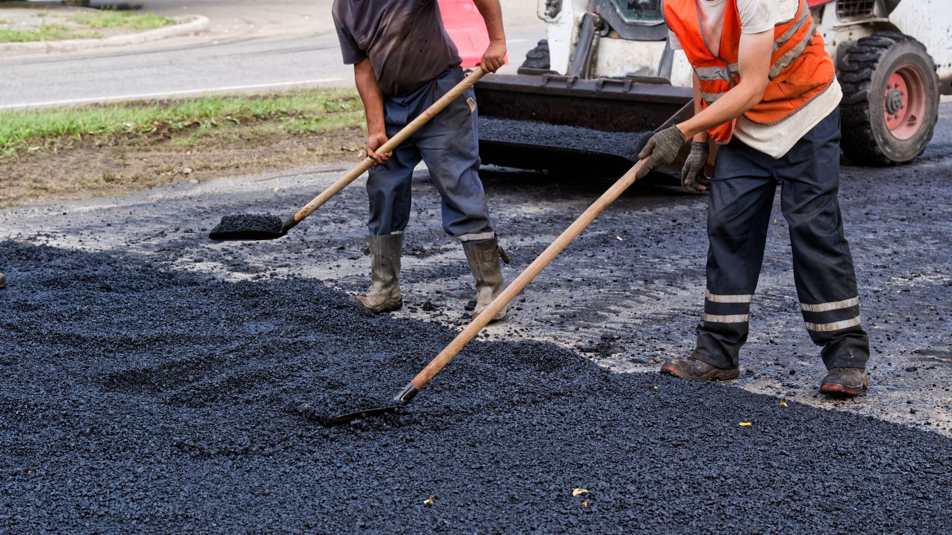 Asphalt resurfacing contractors representing crew leveling fresh asphalt with rakes and shovels.