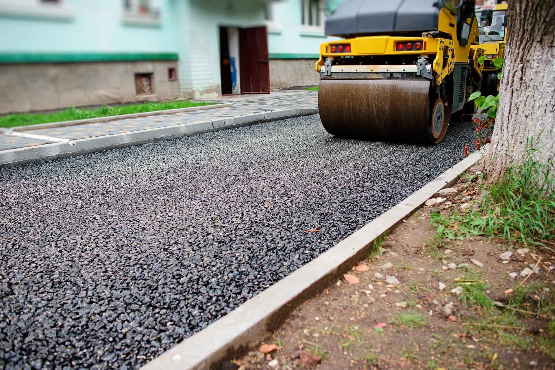 Fresh asphalt being compacted by a road roller on a residential street.