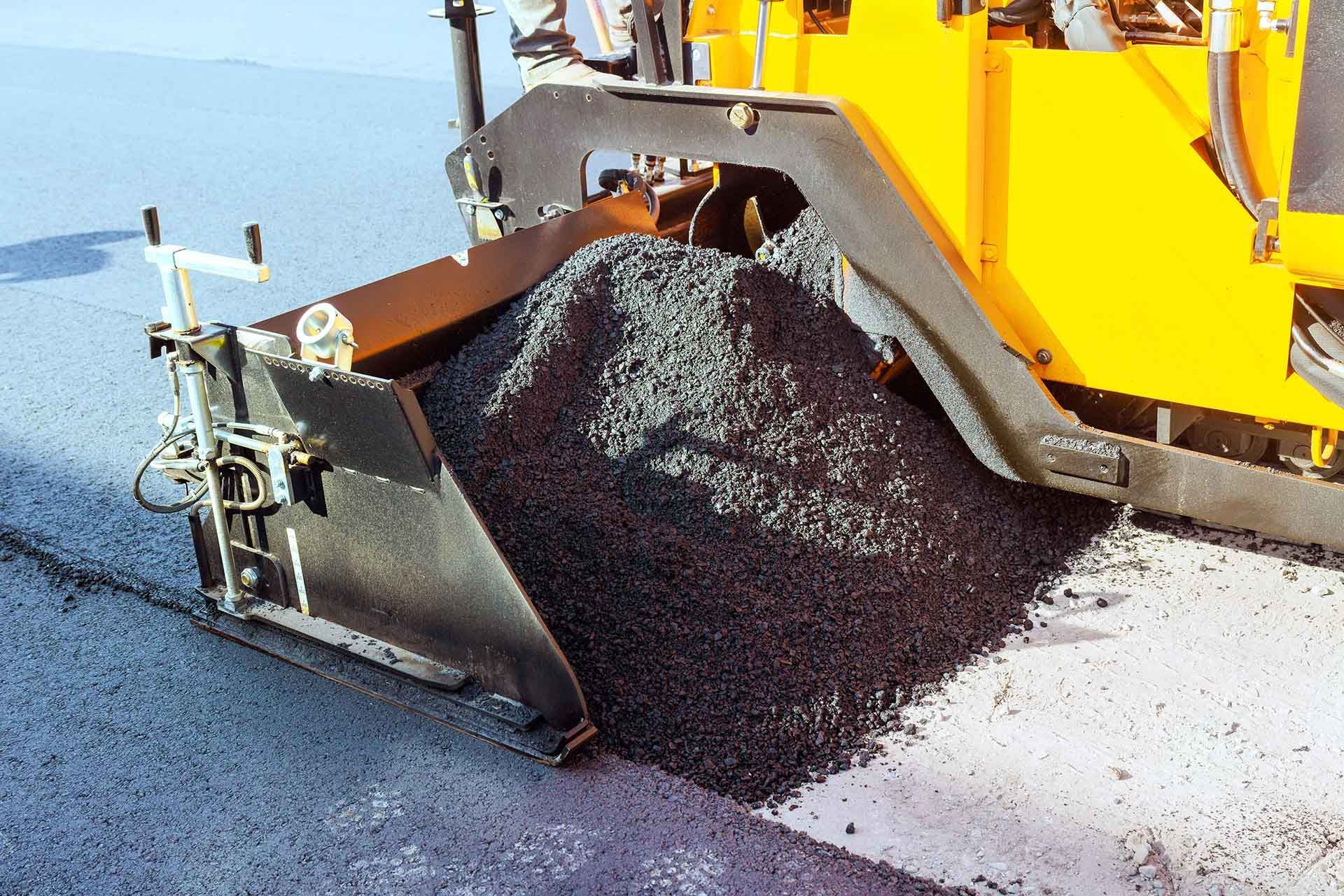 Asphalt paver spreading fresh hot mix over a roadway during paving work. Asphalt paver spreading fresh hot mix over a roadway during paving work.